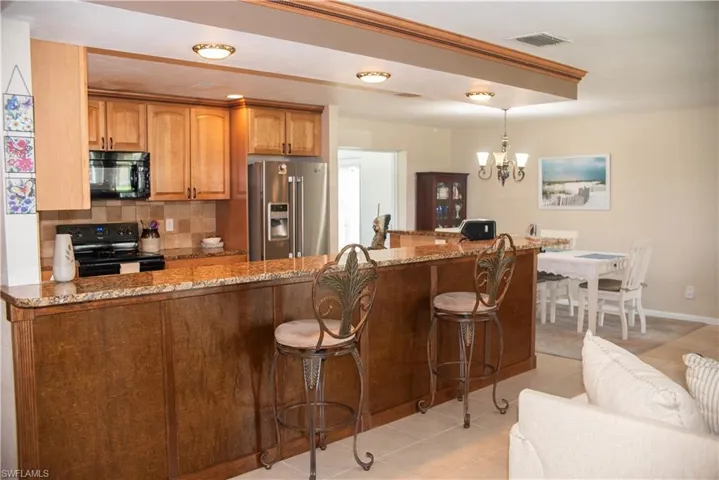 Kitchen with light tile patterned floors, black appliances, tasteful backsplash, and stone countertops