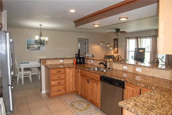 Kitchen with stone counters, ceiling fan with notable chandelier, sink, appliances with stainless steel finishes, and kitchen peninsula