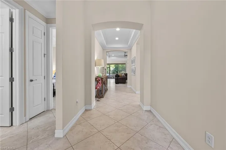 Arched entryway leading to an interior hallway with light tile flooring, recessed lighting, and crown molding