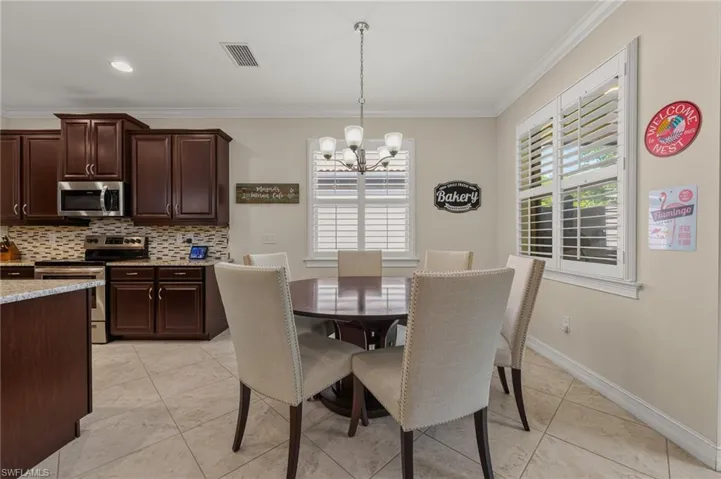 Dining area featuring a circular wood-finish table with upholstered chairs, tiled flooring, plantation shutters, and a chandelier