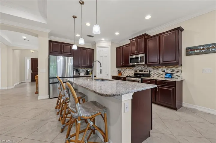 Kitchen featuring dark wood cabinetry, stainless steel appliances, a tile backsplash, and a large central island with a light-toned countertop