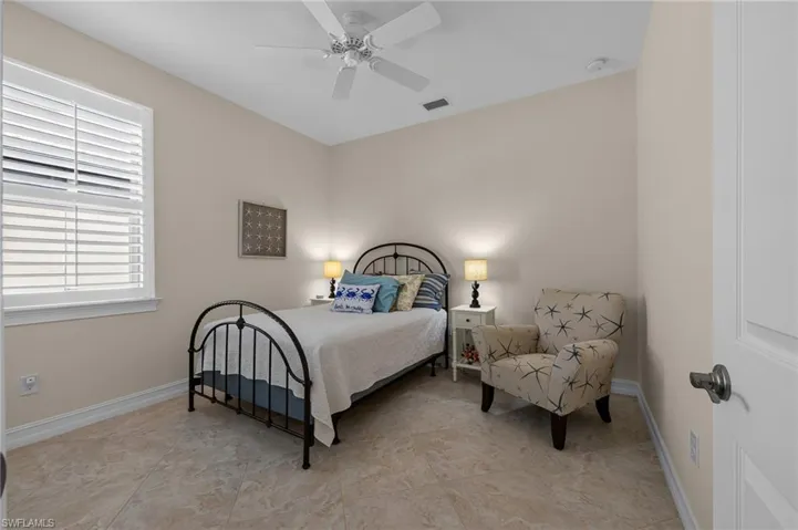 Neutral-toned room featuring large format tile flooring, a window with plantation shutters, a ceiling fan, and white baseboards