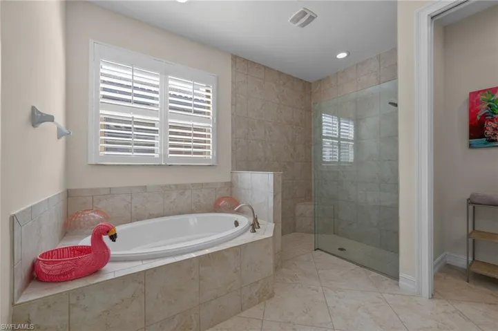 Soaking tub with a tiled surround, plantation shutters, and a separate glass-enclosed shower featuring a tiled bench