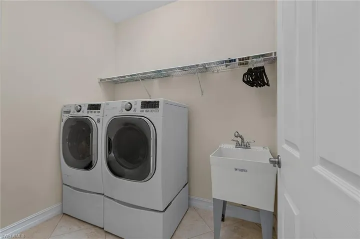 Dedicated utility room featuring floor-mounted laundry appliances, a utility sink with faucet, and wire shelving