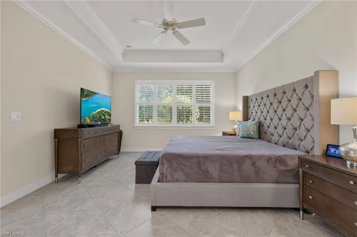 Tray ceiling with crown molding and a ceiling fan, featuring a window with white plantation shutters and light tile flooring