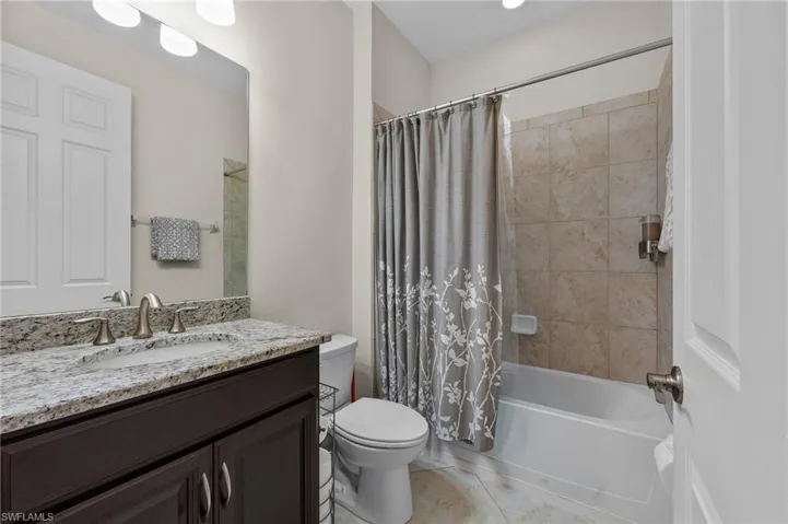Bathroom featuring a dark wood-finish vanity with a light granite countertop, undermount sink, and brushed nickel fixtures