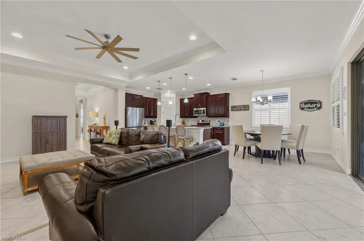 Expansive open-concept living area featuring tray ceilings with recessed lighting, an oversized ceiling fan, and large format tile flooring
