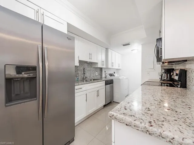 Kitchen featuring stainless steel appliances, washer and clothes dryer, a sink, ornamental molding, and backsplash