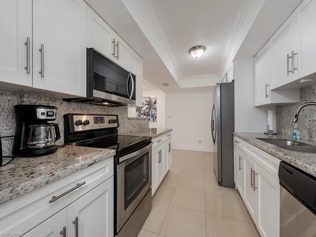Kitchen featuring stainless steel appliances, a sink, ornamental molding, a raised ceiling, and backsplash