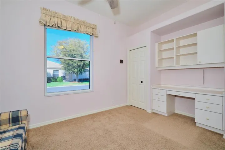 Unfurnished office with light carpet, built in desk, and ceiling fan