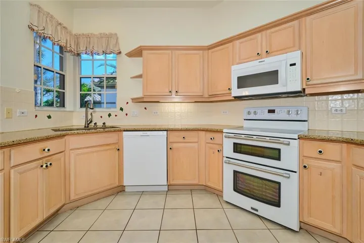 Kitchen with light wood finish cabinets, white appliances, light stone counters, light tile patterned flooring, and open shelves