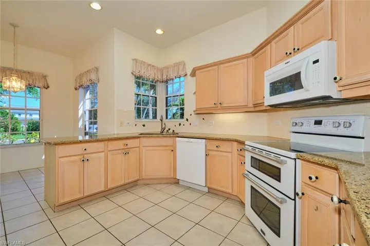 Kitchen with white appliances, light wood finish cabinets, light stone counters, tasteful backsplash, and light tile patterned floors