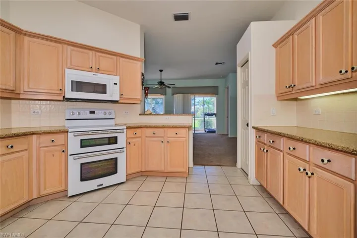 Kitchen with light wood finish cabinetry, tasteful backsplash, white appliances, and a peninsula