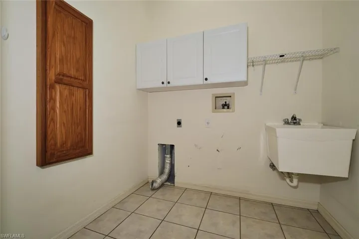 Laundry area with cabinet space, electric dryer hookup, light tile patterned floors, and washer hookup