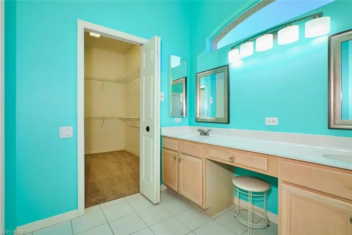 Bathroom with double vanity, light carpet, light tile patterned floors, and a spacious closet