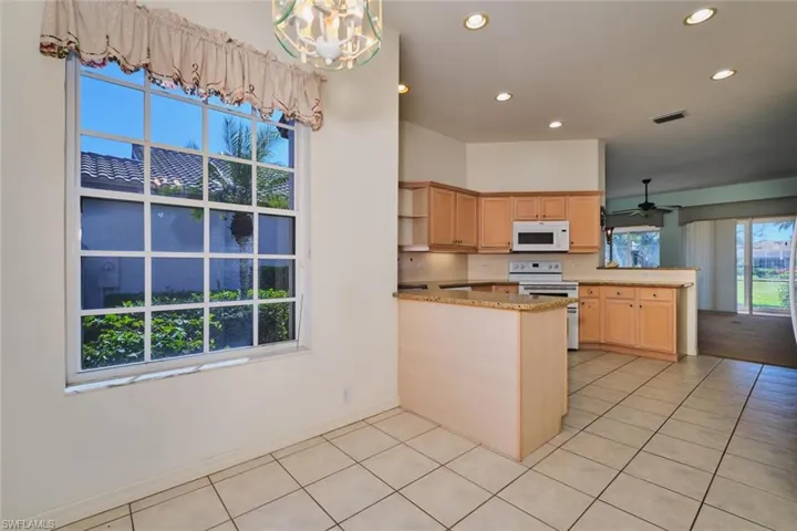 Kitchen with a peninsula, white appliances, light wood finish cabinets, and recessed lighting