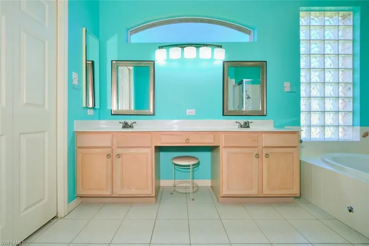 Full bathroom featuring double vanity, a garden tub, light tile patterned flooring, and plenty of natural light