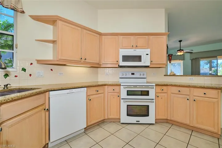 Kitchen with light wood finish cabinetry, white appliances, light stone countertops, and tasteful backsplash