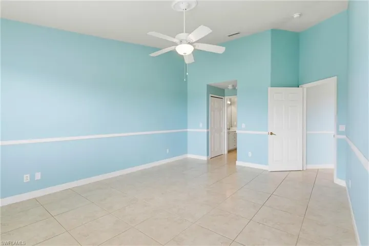 Unfurnished bedroom with a ceiling fan, a closet, light tile patterned floors, ensuite bath, and a high ceiling