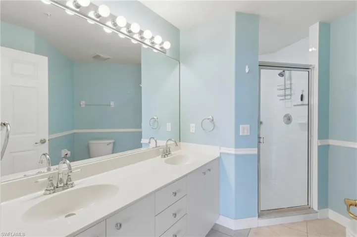 Bathroom featuring a shower stall, double vanity, and light tile patterned floors
