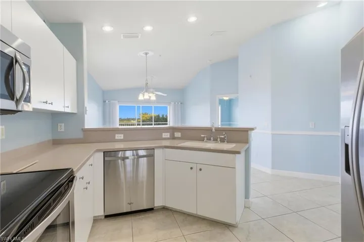 Kitchen with stainless steel appliances, white cabinets, a peninsula, light countertops, and vaulted ceiling