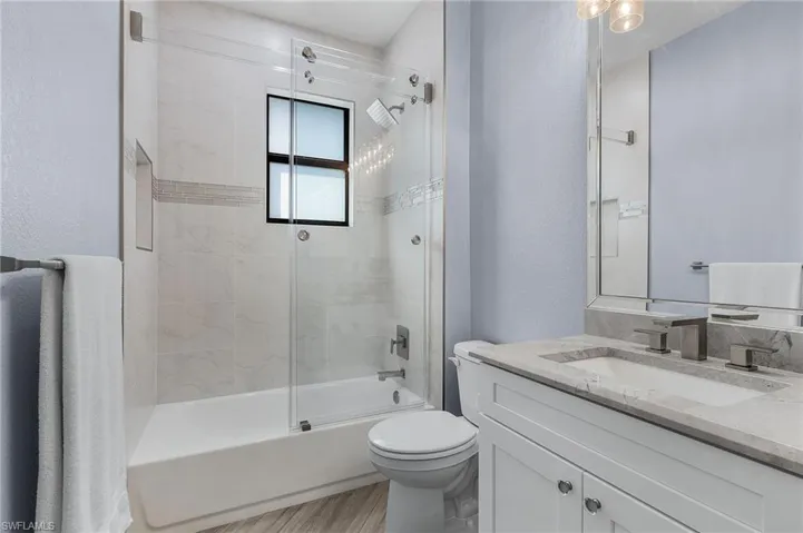 Full bathroom featuring vanity, wood-type flooring, enclosed tub / shower combo, and toilet