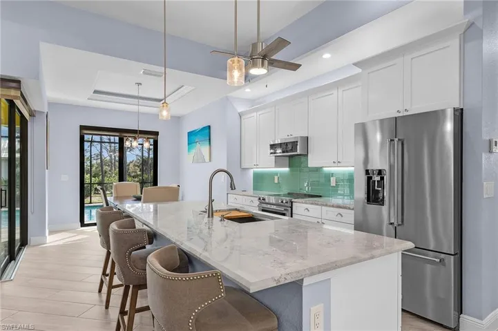 Kitchen featuring hanging light fixtures, high quality appliances, white cabinets, a center island with sink, and a raised ceiling