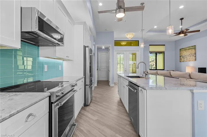 Kitchen with pendant lighting, an island with sink, sink, white cabinets, and stainless steel appliances