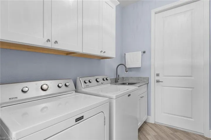 Laundry room featuring light hardwood / wood-style floors, cabinets, separate washer and dryer, and sink