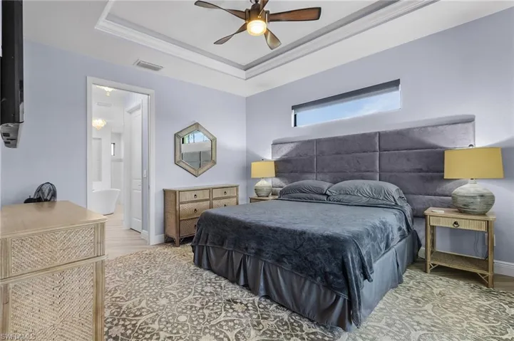 Bedroom featuring connected bathroom, ceiling fan, and a tray ceiling
