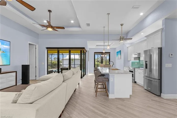 Kitchen with decorative light fixtures, a center island with sink, a raised ceiling, stainless steel appliances, and white cabinets