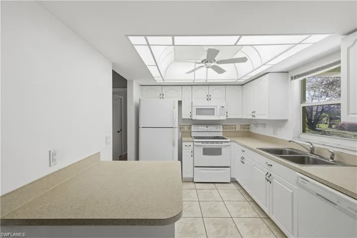 Kitchen featuring white appliances, light countertops, white cabinets, light tile patterned floors, and a ceiling fan