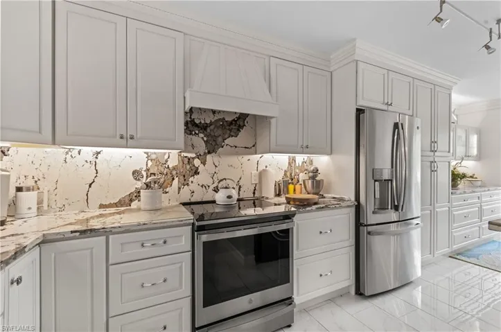 Gourmet kitchen featuring light cabinetry, stainless steel appliances, a range oven, under-cabinet lighting, and a unique natural stone Quartz backsplash extending to the countertops