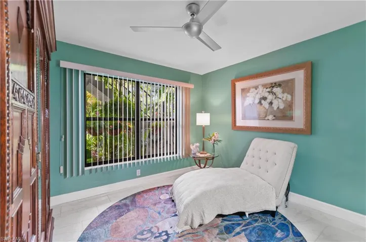 Bedroom currently used as a sitting area featuring a large window with vertical blinds, a ceiling fan, light aqua walls, and white baseboards