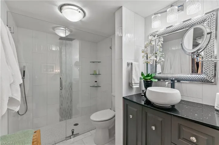 Updated bathroom featuring a spacious glass-enclosed shower with a rainfall showerhead, a dark wood-finish vanity and beautiful  lighting