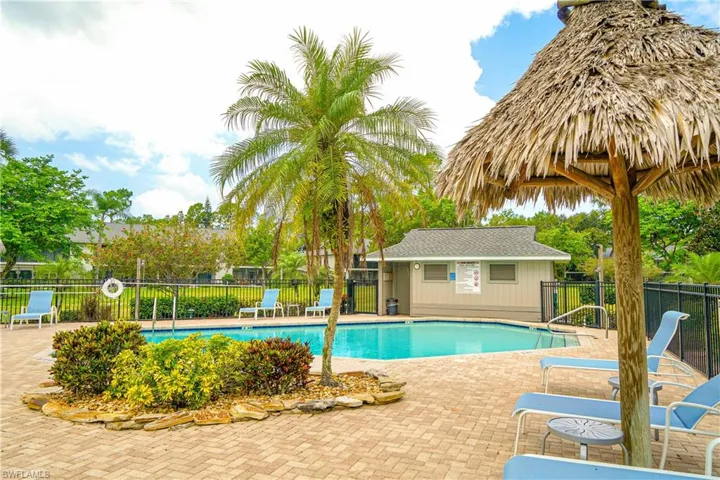 Resort-style pool area featuring a paver deck, mature palm trees, a thatched umbrella, and a pool bath
