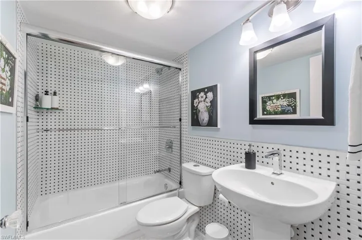 Newer bathroom featuring a white pedestal sink, toilet, and bathtub with a glass shower enclosure
