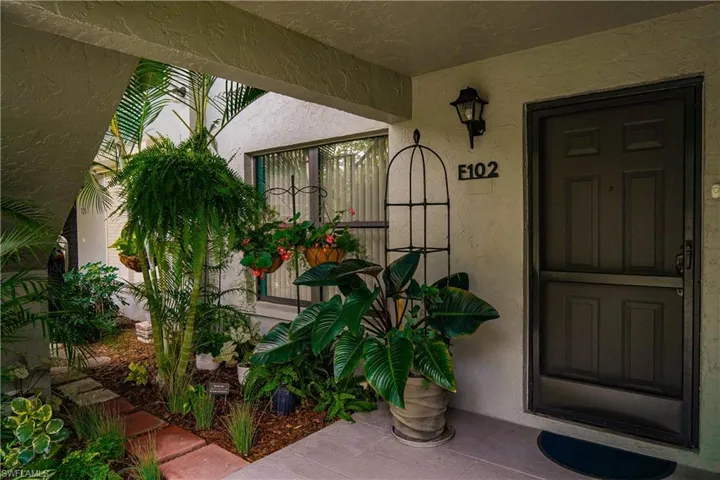 Entryway featuring a dark paneled door with a screen door, sconce lighting, and a garden bed with stepping stones
