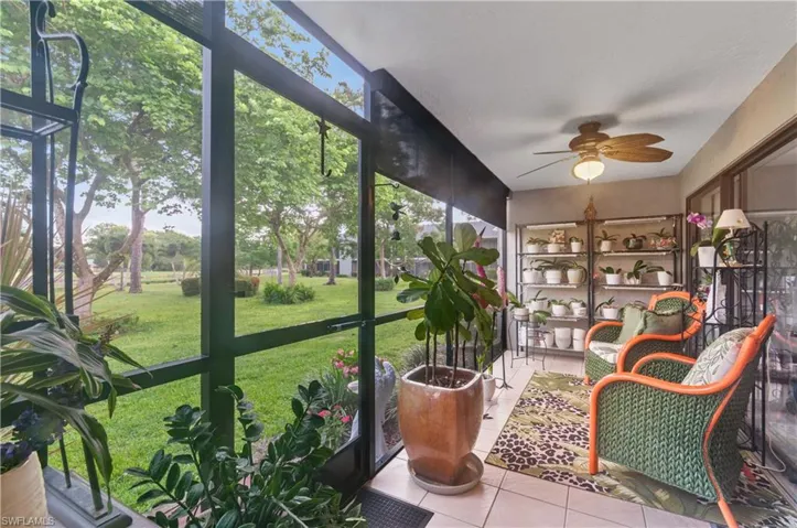 Screened patio lanai with tile flooring and a ceiling fan, overlooking a verdant lawn and mature trees