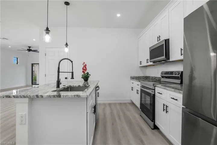 Kitchen with stainless steel appliances, light wood finished floors, an island with sink, white cabinetry, and light stone counters