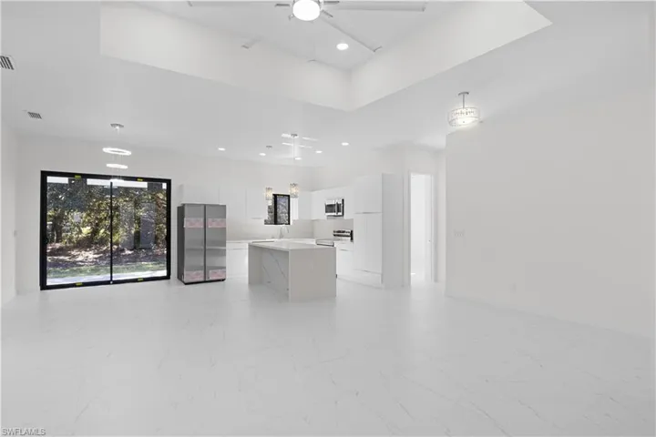 Kitchen with white cabinets, a tray ceiling, open floor plan, stainless steel appliances, and recessed lighting
