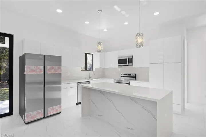 Kitchen featuring modern cabinets, stainless steel appliances, white cabinets, light marble finish floors, and recessed lighting