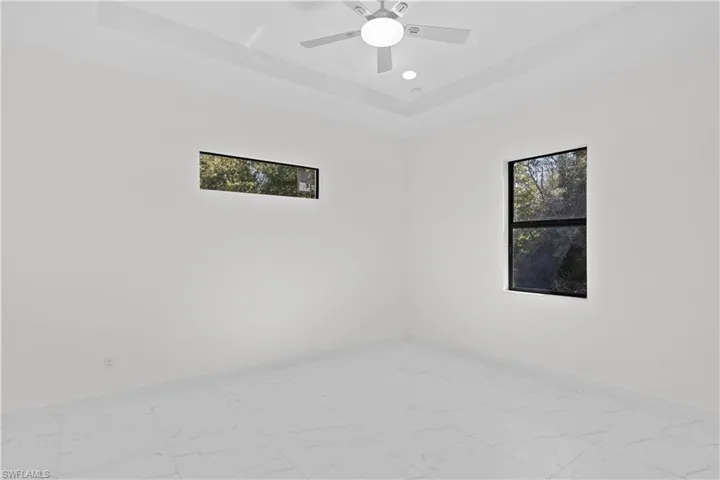 Empty room featuring plenty of natural light, a raised ceiling, light marble finish floors, and recessed lighting