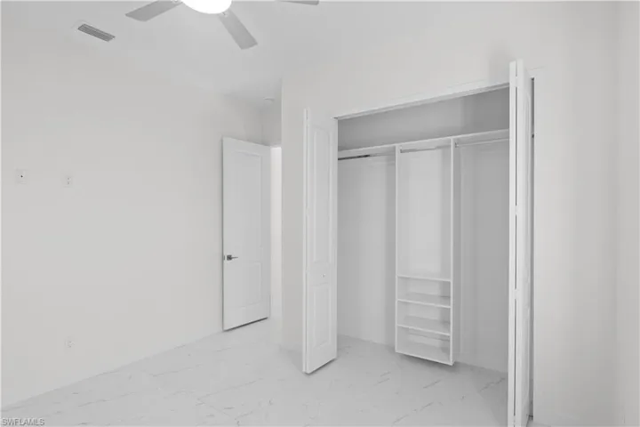 Unfurnished bedroom featuring light marble finish flooring, a ceiling fan, and a closet