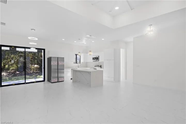 Kitchen featuring decorative light fixtures, white cabinetry, open floor plan, light marble finish flooring, and a kitchen island