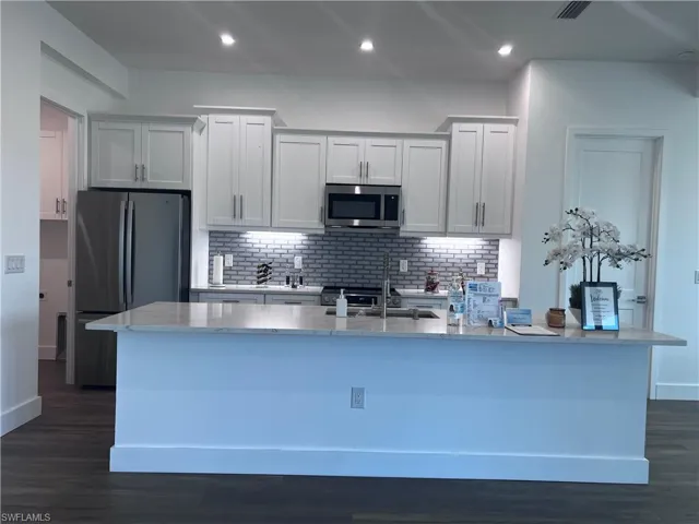 Contemporary kitchen featuring a large island with a light-colored countertop, white shaker-style cabinetry, stainless steel appliances, a subway tile backsplash, and recessed lighting