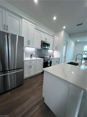 Modern kitchen featuring white shaker cabinetry, stainless steel appliances, wood-finish flooring, a mosaic tile backsplash, and a large island with a light-toned countertop