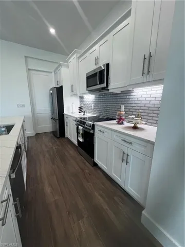 Modern kitchen featuring white shaker cabinetry, stainless steel appliances, a subway tile backsplash, light stone countertops, and wood-finish flooring