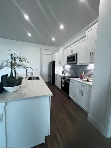 Gourmet kitchen featuring a substantial island with an integrated sink and light-toned countertop, wood-finish flooring, white shaker-style cabinetry, and stainless steel appliances