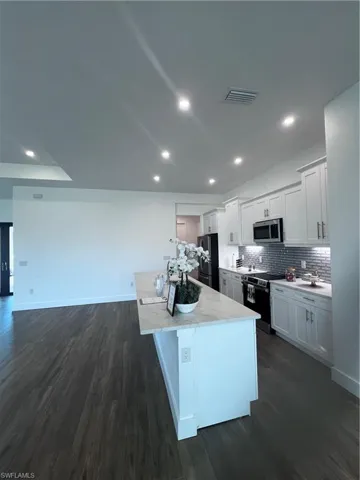 Kitchen featuring a central island with a light-toned countertop, white cabinetry with silver-toned hardware, a gray subway tile backsplash, recessed lighting, and dark wood-finish flooring